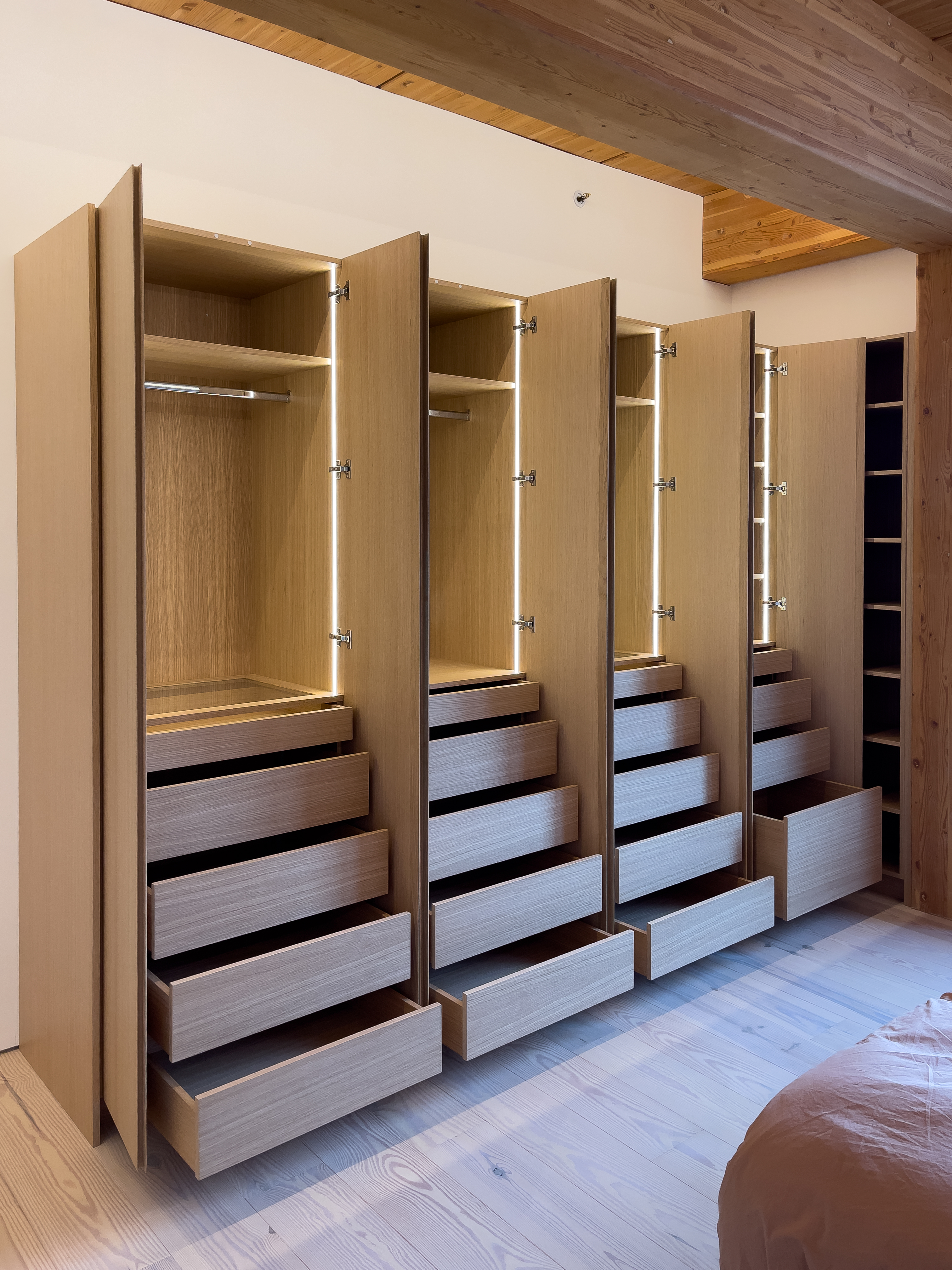 Full-wall white oak wardrobe with open doors showing LED-lit interior and stacked drawers