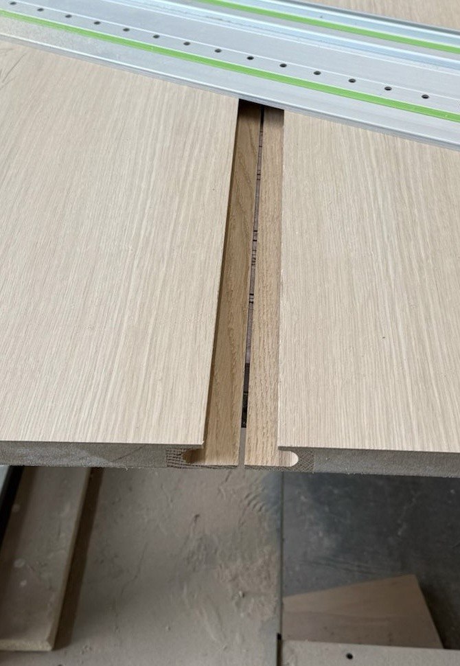 A full-height solid white oak finger pull cut into the door between two oak panels, photographed from the inside before the edge is covered. Wewillbebirds millwork detail