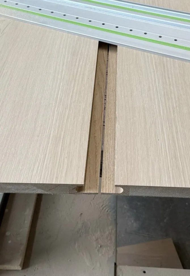 A full-height solid white oak finger pull cut into the door between two oak panels, photographed from the inside before the edge is covered. Wewillbebirds millwork detail