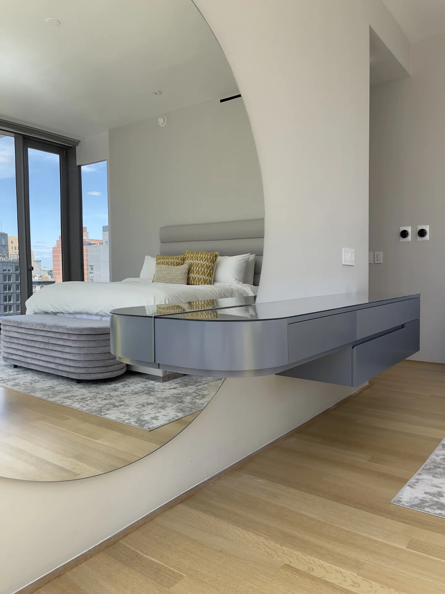 Floating console's curved end in front of the six-foot mirror, bed reflected, Tribeca high-rise bedroom