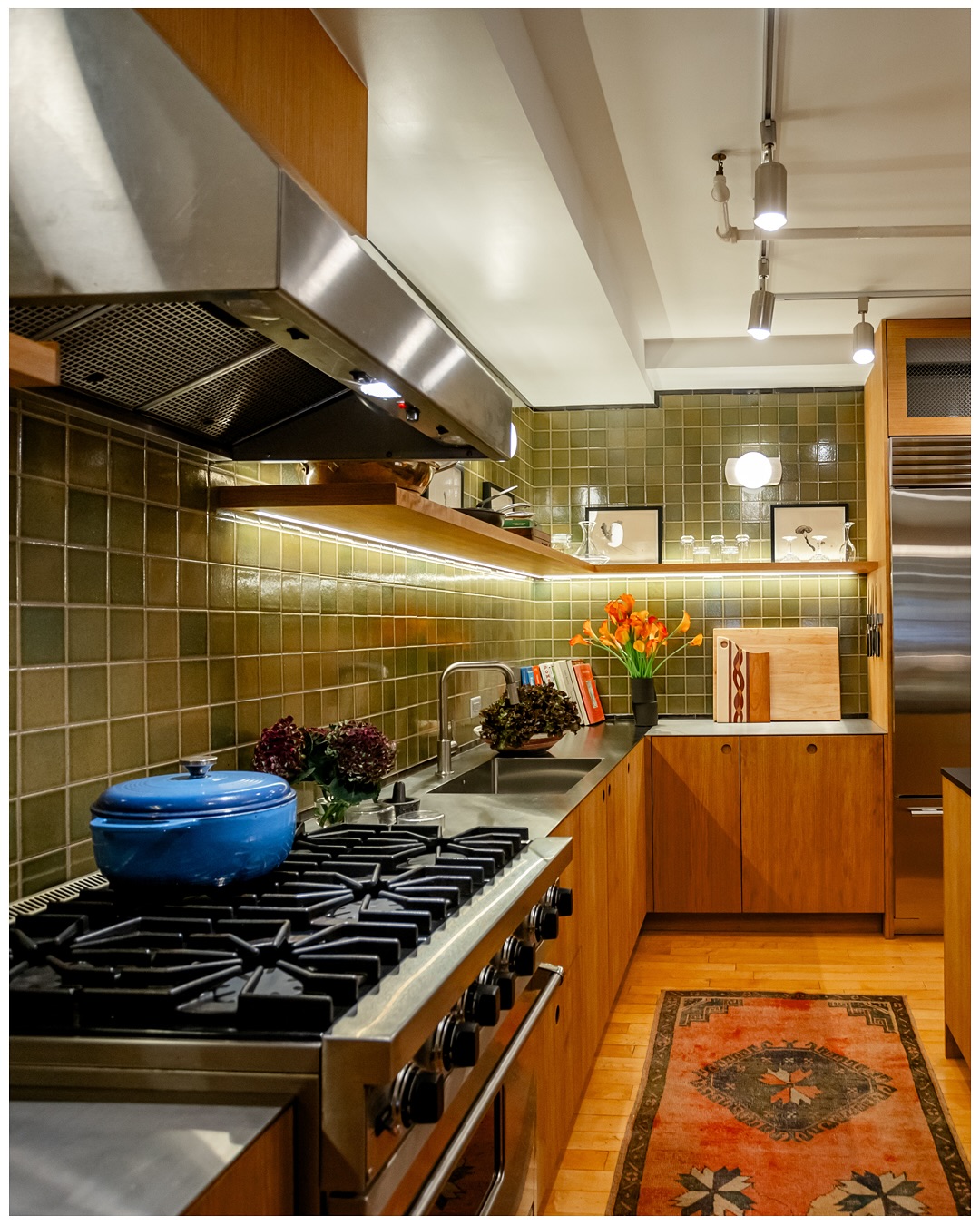 Professional range under green glazed tile, framed by wood cabinets and a patterned rug