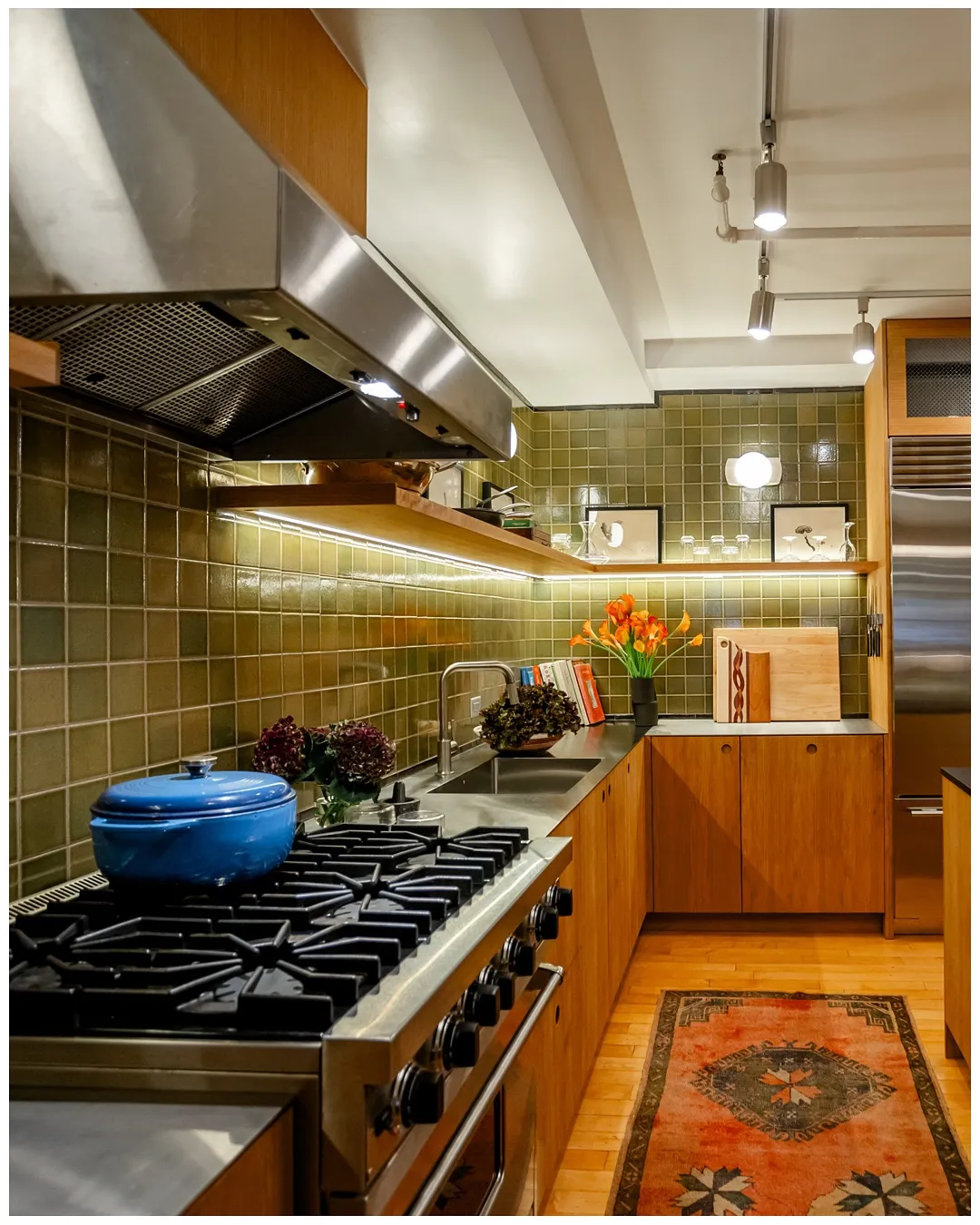 Professional range under green glazed tile, framed by wood cabinets and a patterned rug