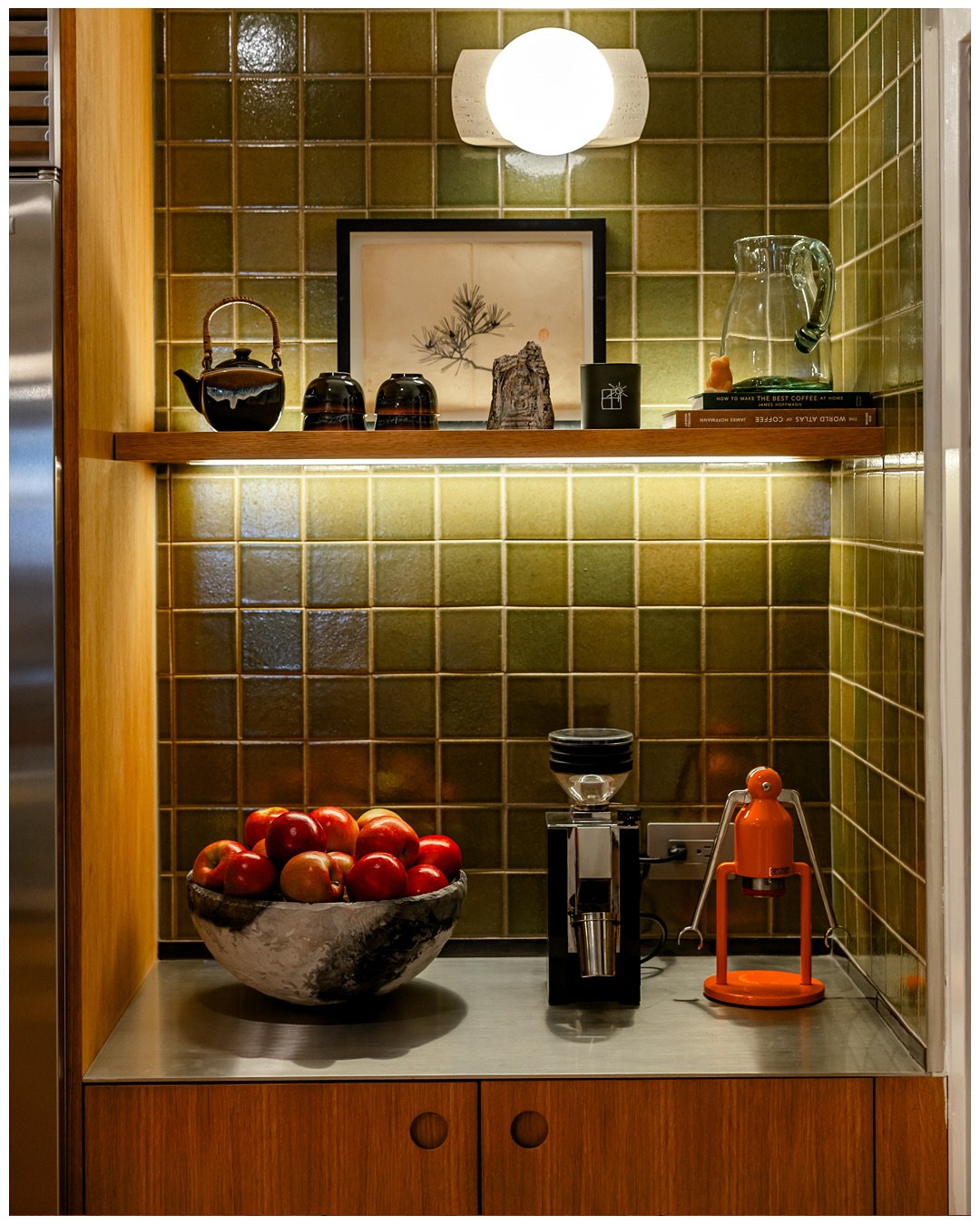 Floating shelf with a tea set and framed art above a stone counter and coffee station