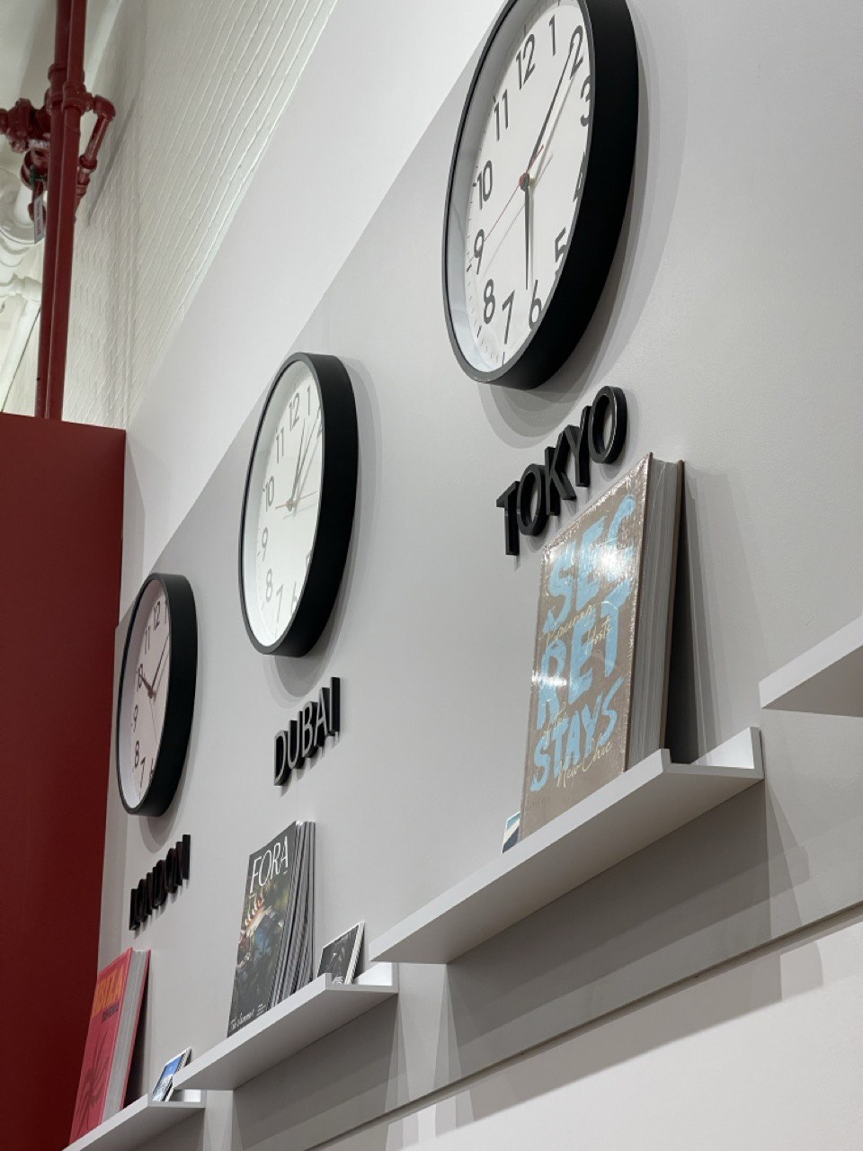 Floating shelf below a wall of clocks holding magazines and travel titles
