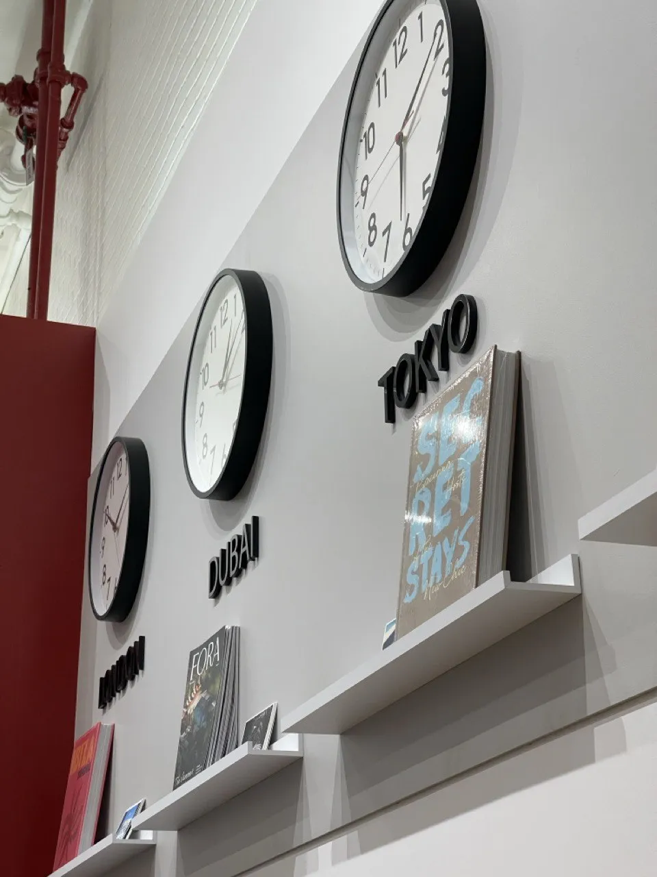 Floating shelf below a wall of clocks holding magazines and travel titles