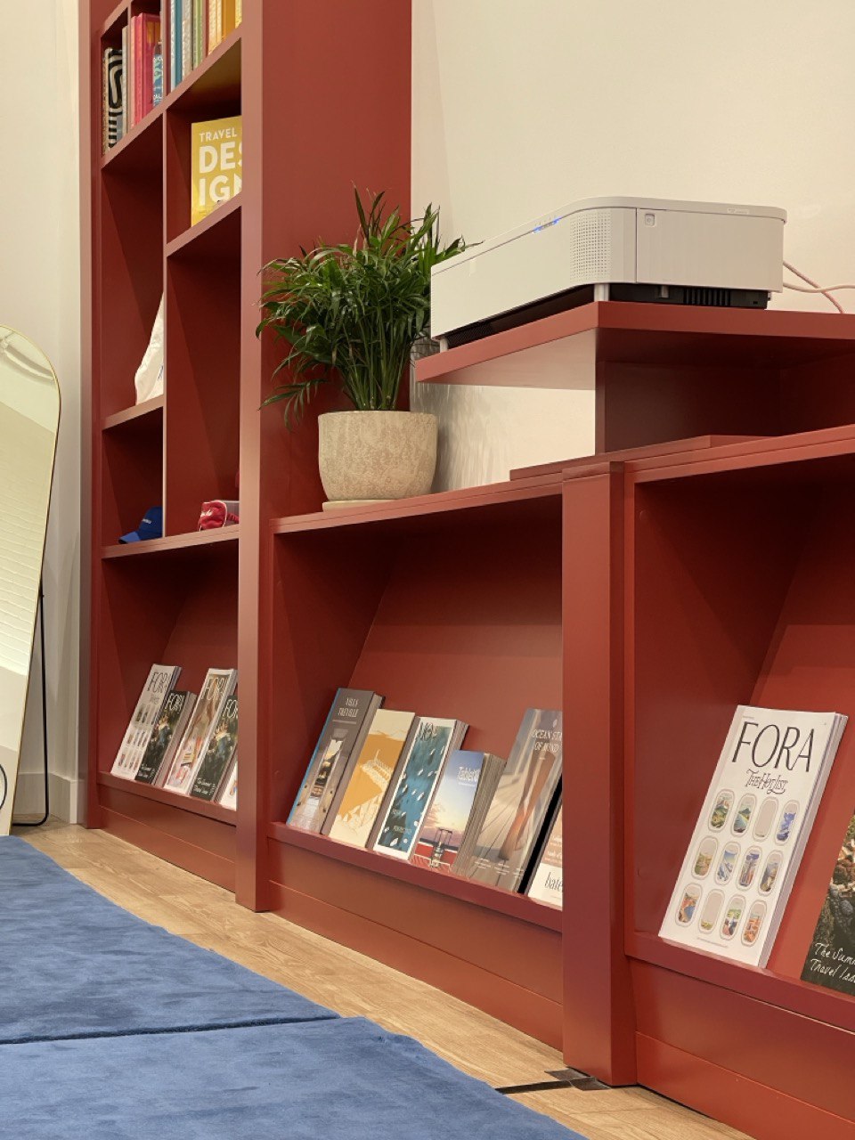 Terracotta shelving with travel magazines, a plant, and the brand’s own edition on display