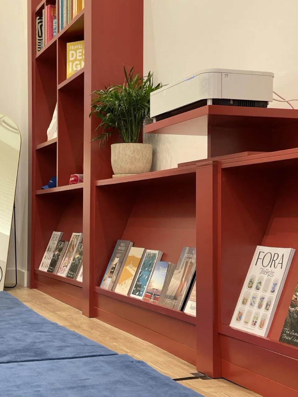 Terracotta shelving with travel magazines, a plant, and the brand’s own edition on display