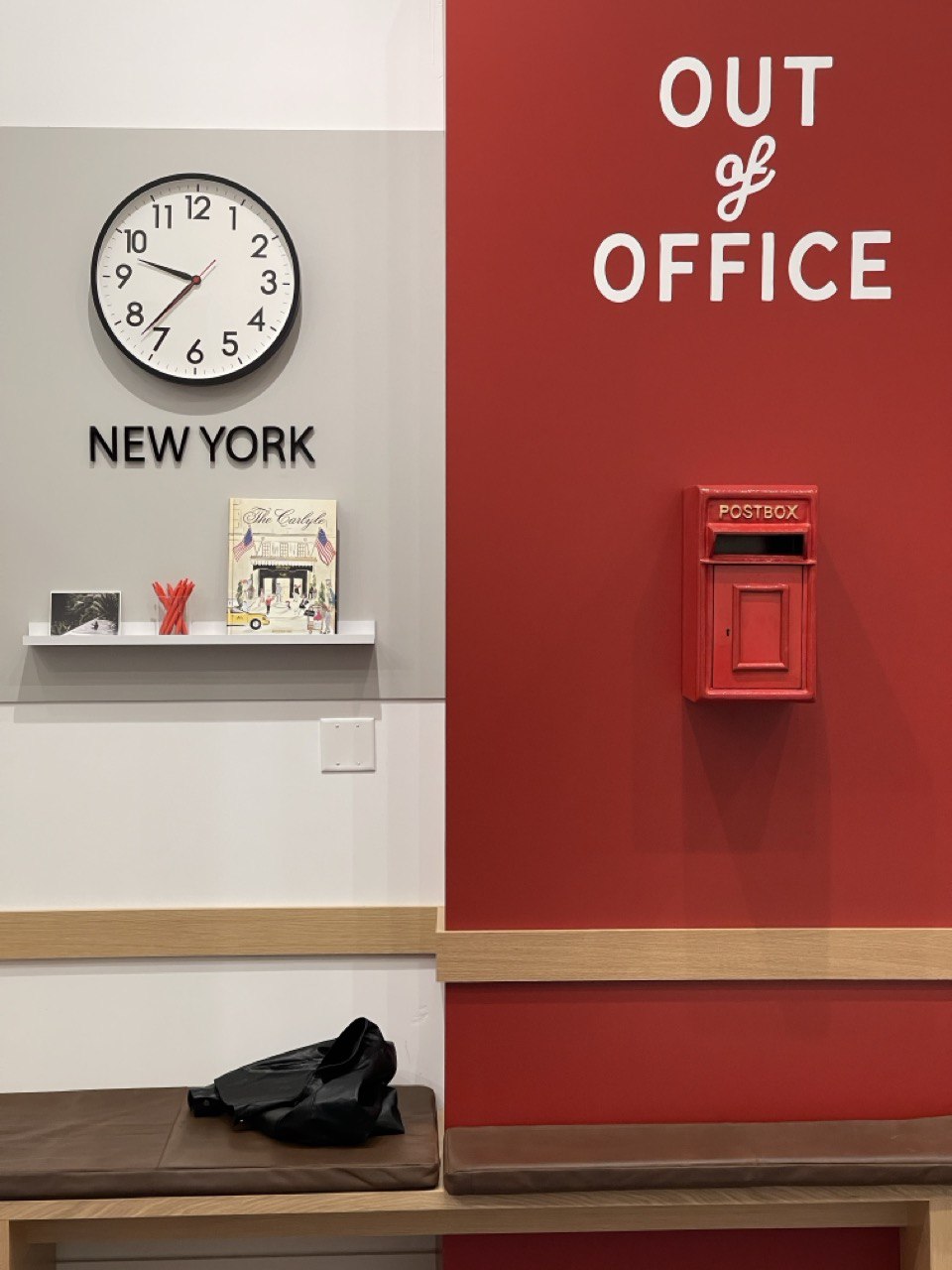 “Out of Office” feature wall with a New York clock, a working red postbox, and bench seating